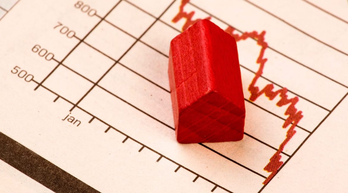 A small red wooden house sits on top of a volatile financial chart, symbolizing the instability and crisis in the Canadian housing market.
