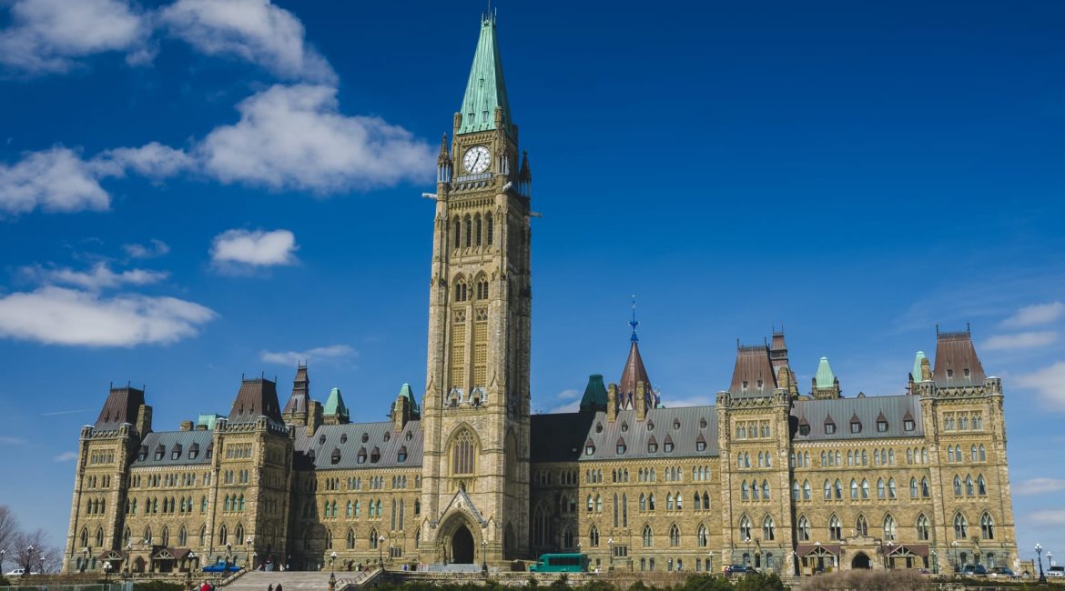 The Centre Block of the Canadian Parliament Buildings in Ottawa on a sunny day, with the Peace Tower prominent against a blue sky with white clouds.