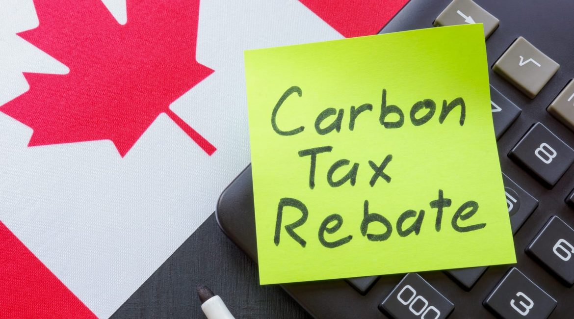 A sticky note with the words 'Carbon Tax Rebate' written on it sits on a calculator, which is placed on a Canadian flag, symbolizing Canada's financial rebate system for carbon pricing.