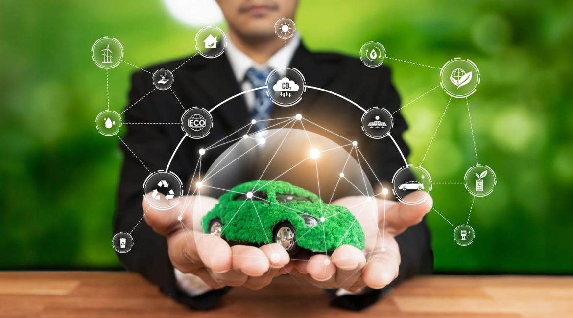 A person in a suit holds out their hands, displaying a car covered in green moss that is surrounded by a web of digital icons for clean energy and sustainability.