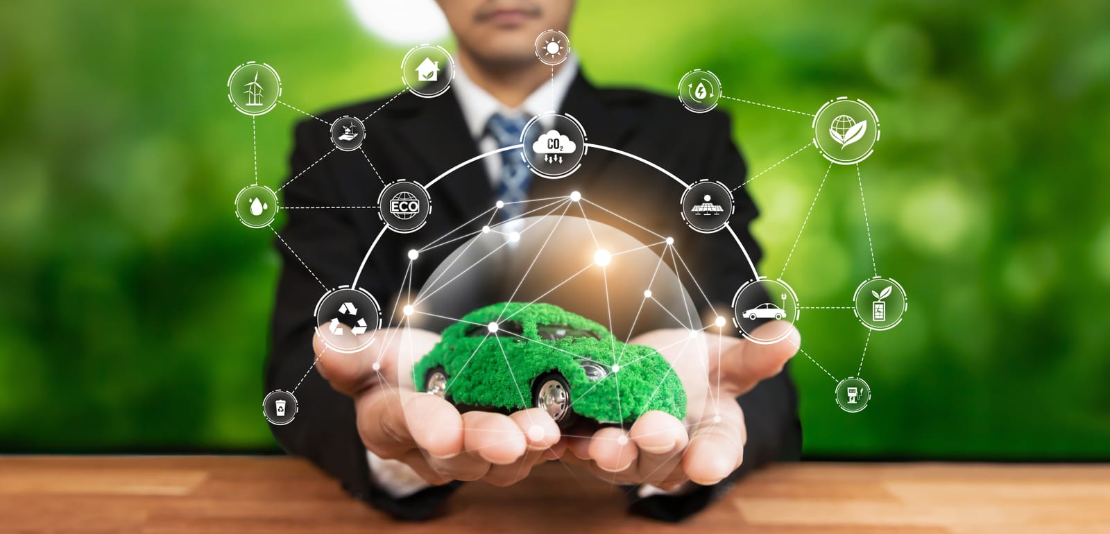 A person in a suit holds out their hands, displaying a car covered in green moss that is surrounded by a web of digital icons for clean energy and sustainability.