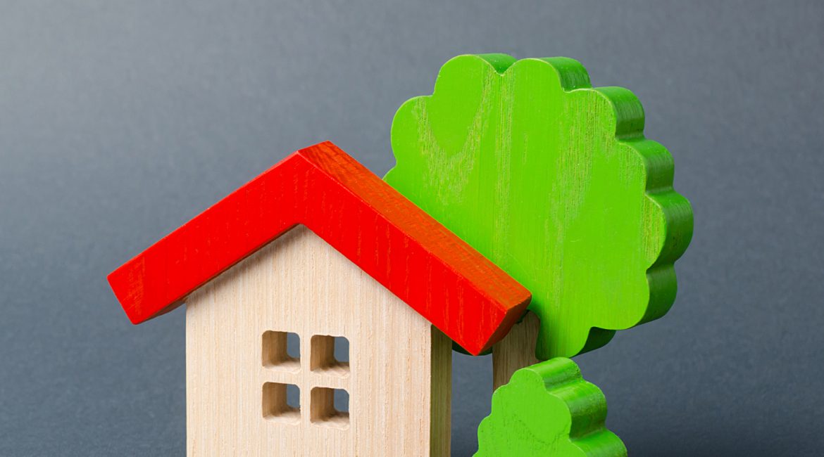 A simple wooden toy house with a red roof next to a green wooden toy tree, symbolizing the core issues of the Canada housing crisis and the dream of home ownership.