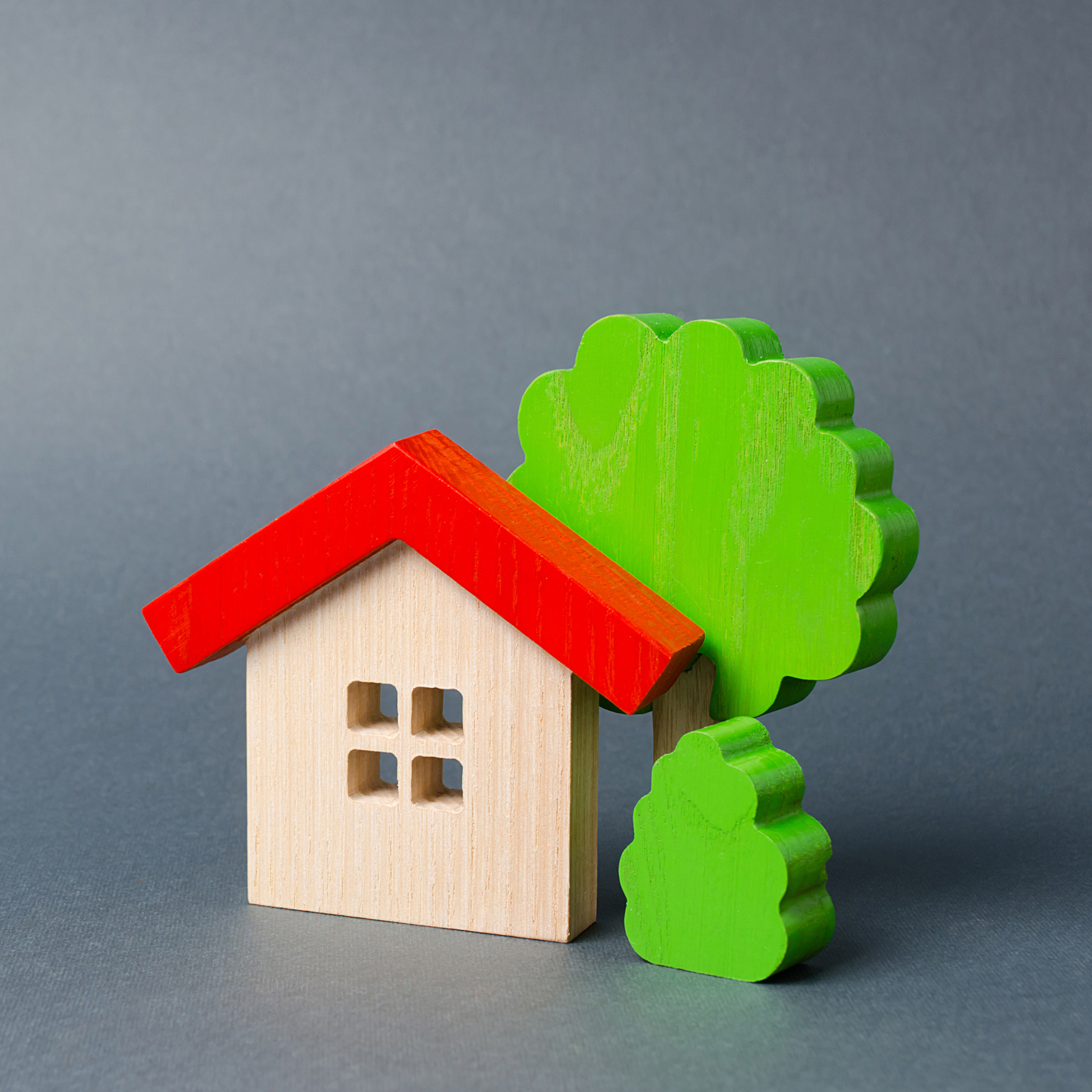 A simple wooden toy house with a red roof next to a green wooden toy tree, symbolizing the core issues of the Canada housing crisis and the dream of home ownership.