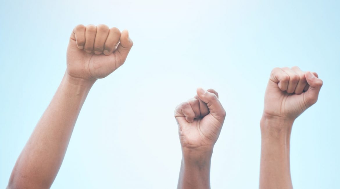 Three raised fists against a clear blue sky, symbolizing the collective power and protection of rights under the Canadian Charter of Rights and Freedoms.