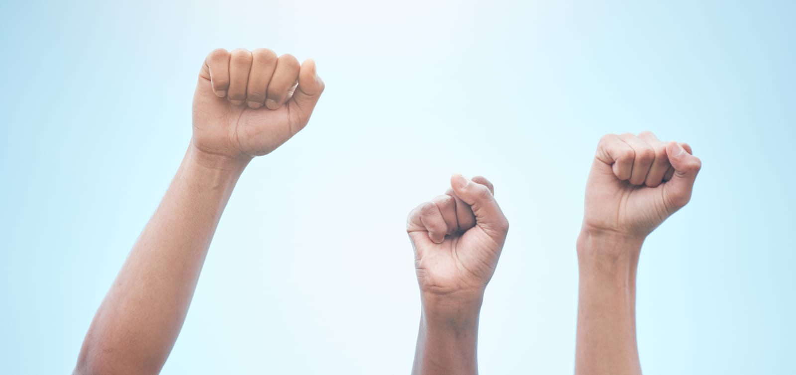 Three raised fists against a clear blue sky, symbolizing the collective power and protection of rights under the Canadian Charter of Rights and Freedoms.