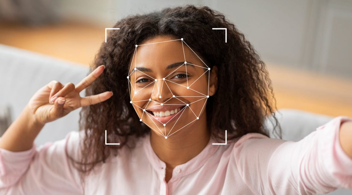 A smiling Black woman takes a selfie, her face overlaid with a digital graphic of facial recognition nodes and lines, representing personal identification technology.