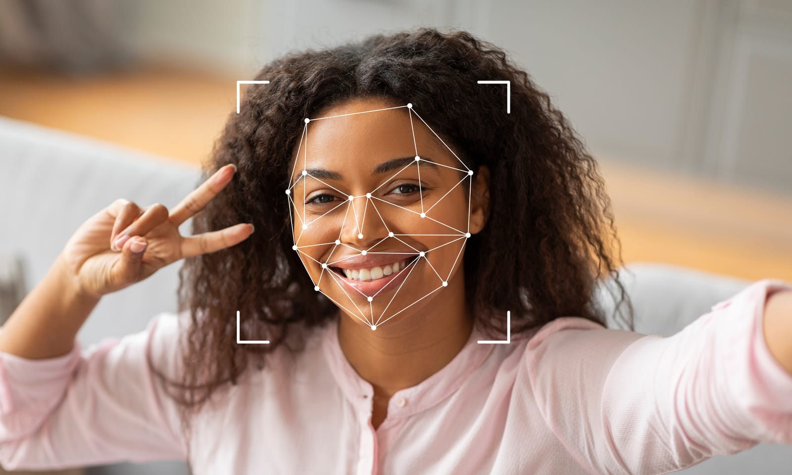 A smiling Black woman takes a selfie, her face overlaid with a digital graphic of facial recognition nodes and lines, representing personal identification technology.
