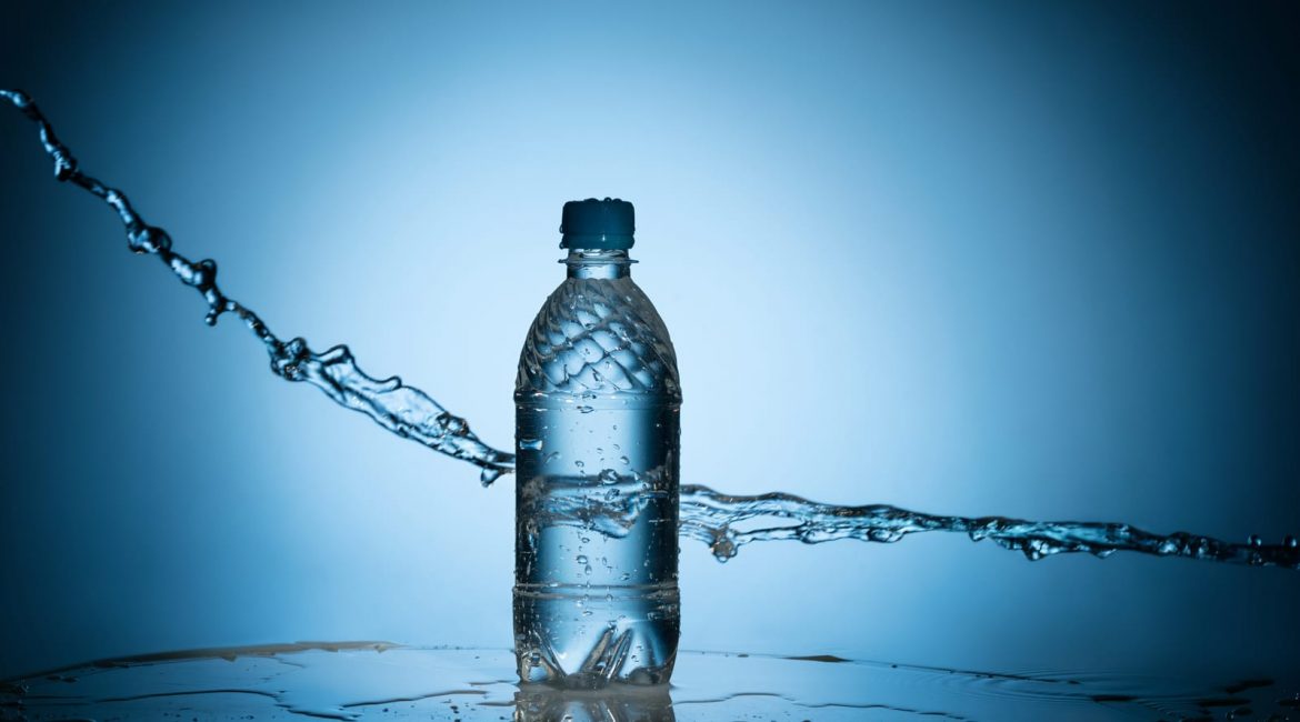 A plastic water bottle sits on a wet surface with water splashing dynamically around it against a blue background, symbolizing the topic of freshwater.