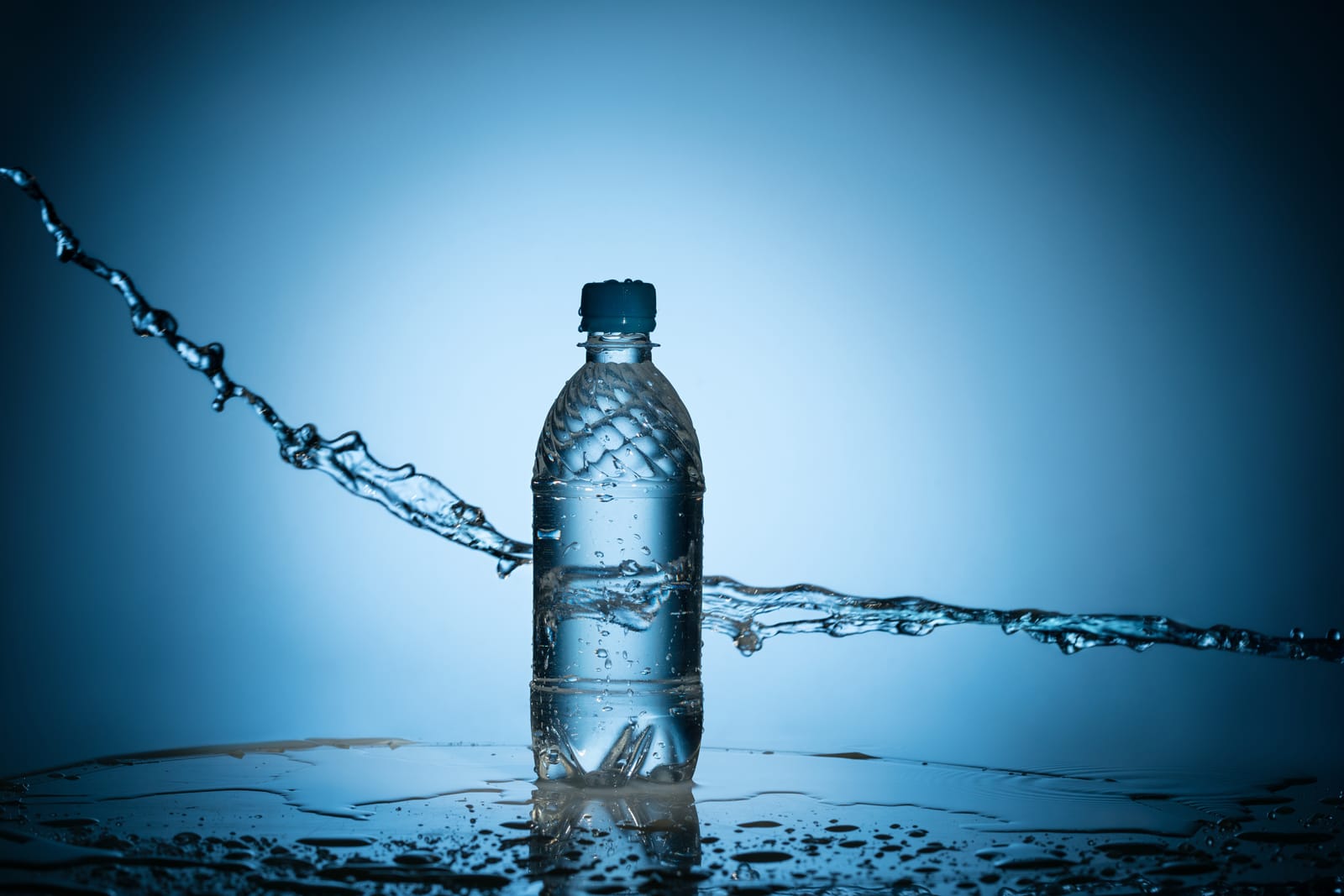 A plastic water bottle sits on a wet surface with water splashing dynamically around it against a blue background, symbolizing the topic of freshwater.