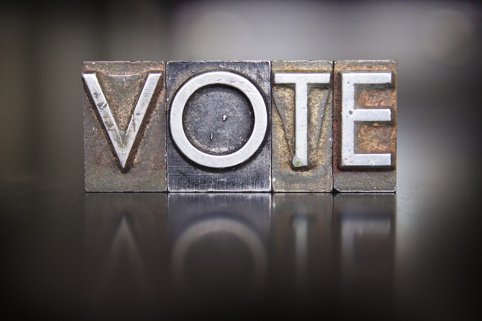 A close-up, artistic shot of old metal letterpress blocks spelling out the word VOTE, representing the topic of elections and electoral reform.