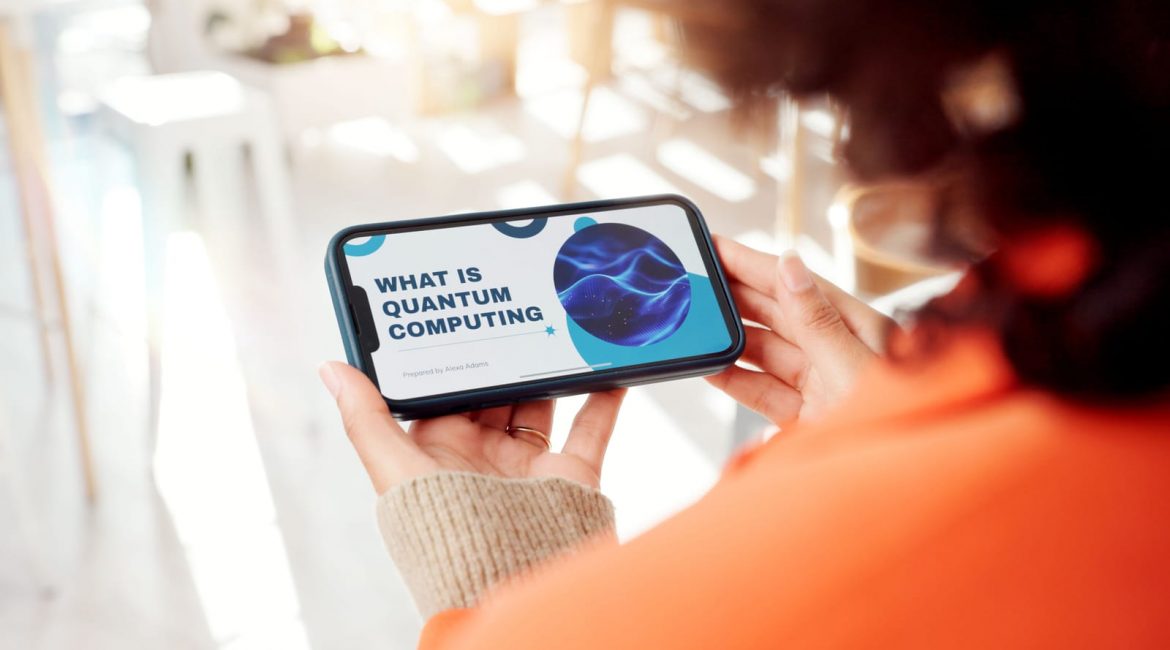 A person holds a smartphone displaying a presentation slide with the title 'What Is Quantum Computing,' representing a modern explanation of the topic.